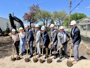 Eight people in hard hats shoveling dirt at Collective groundbreaking event