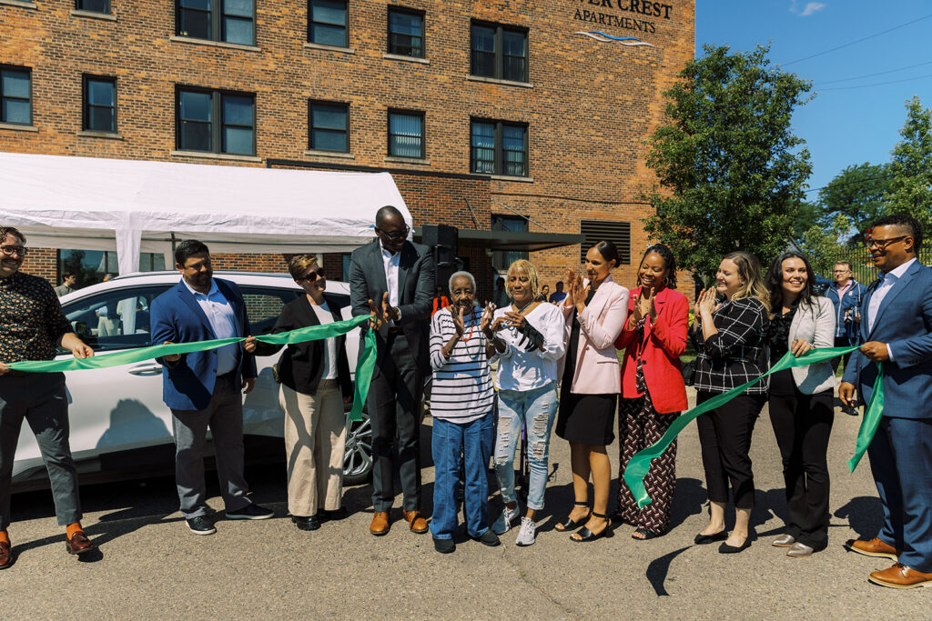 Dignitaries at ribbon cutting in front of EV car and River Crest Apartments