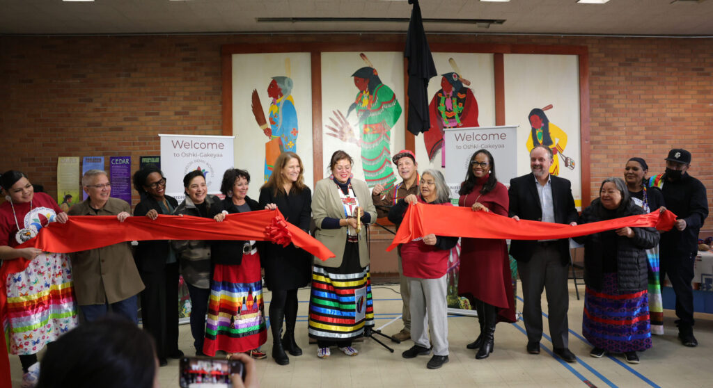 Development partners and Native American women in bright clothing cut a red ribbon
