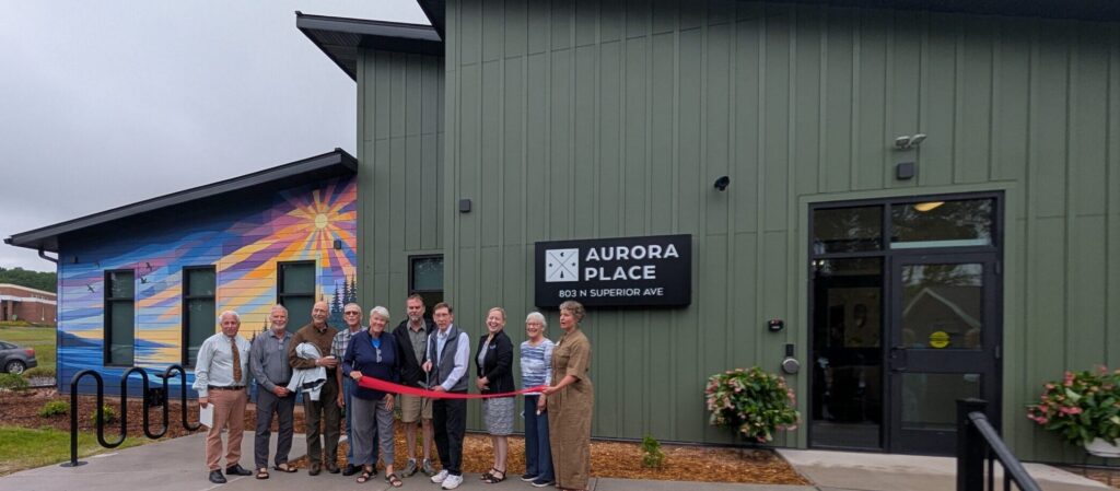 Dignitaries cutting ribbon in front of green apartment building with sunrise mural
