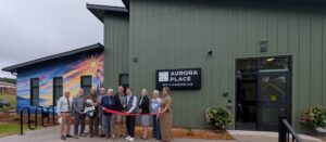 Dignitaries cutting ribbon in front of green apartment building with sunrise mural